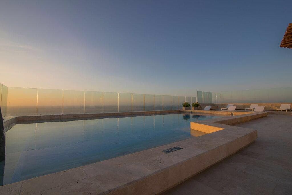 Piscina en la terraza del edificio al atardecer, con vista abierta al mar.