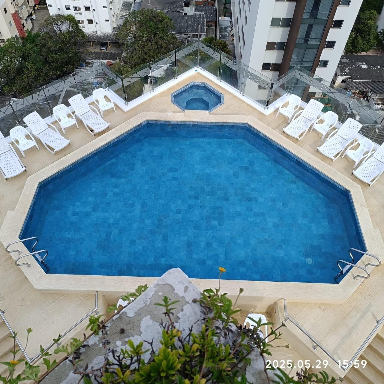 Piscina del edificio vista desde arriba, con jacuzzi y asoleadoras blancas alrededor.