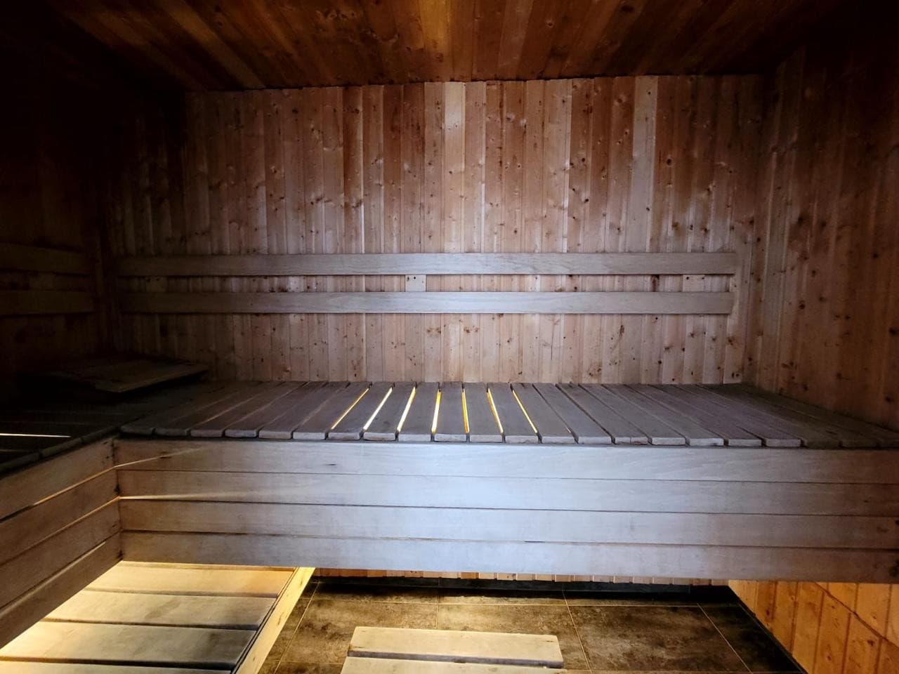 Sauna de madera del edificio, con bancas y piso de listones.