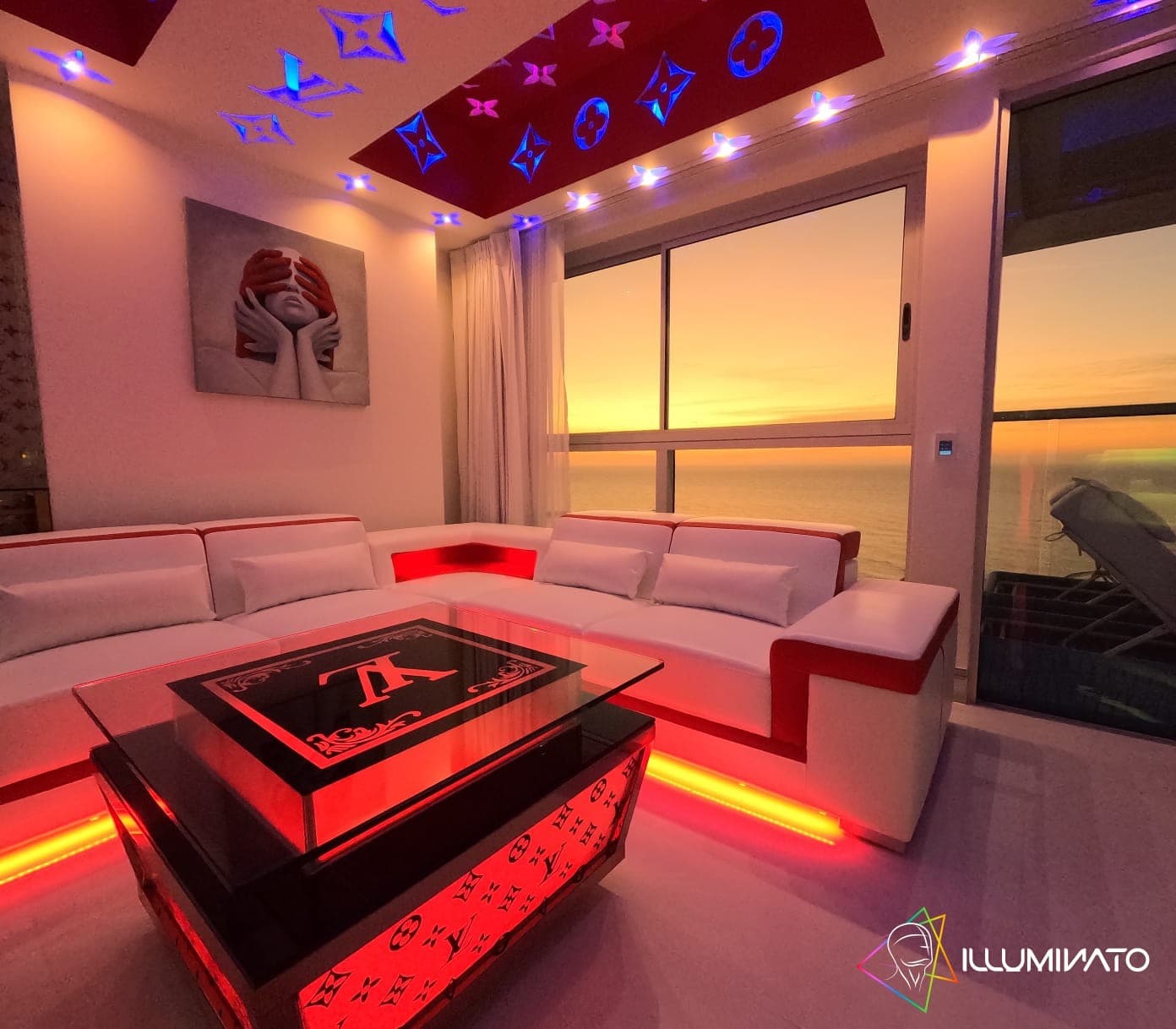 Sala con sofá modular blanco frente al ventanal, con el atardecer sobre el mar.