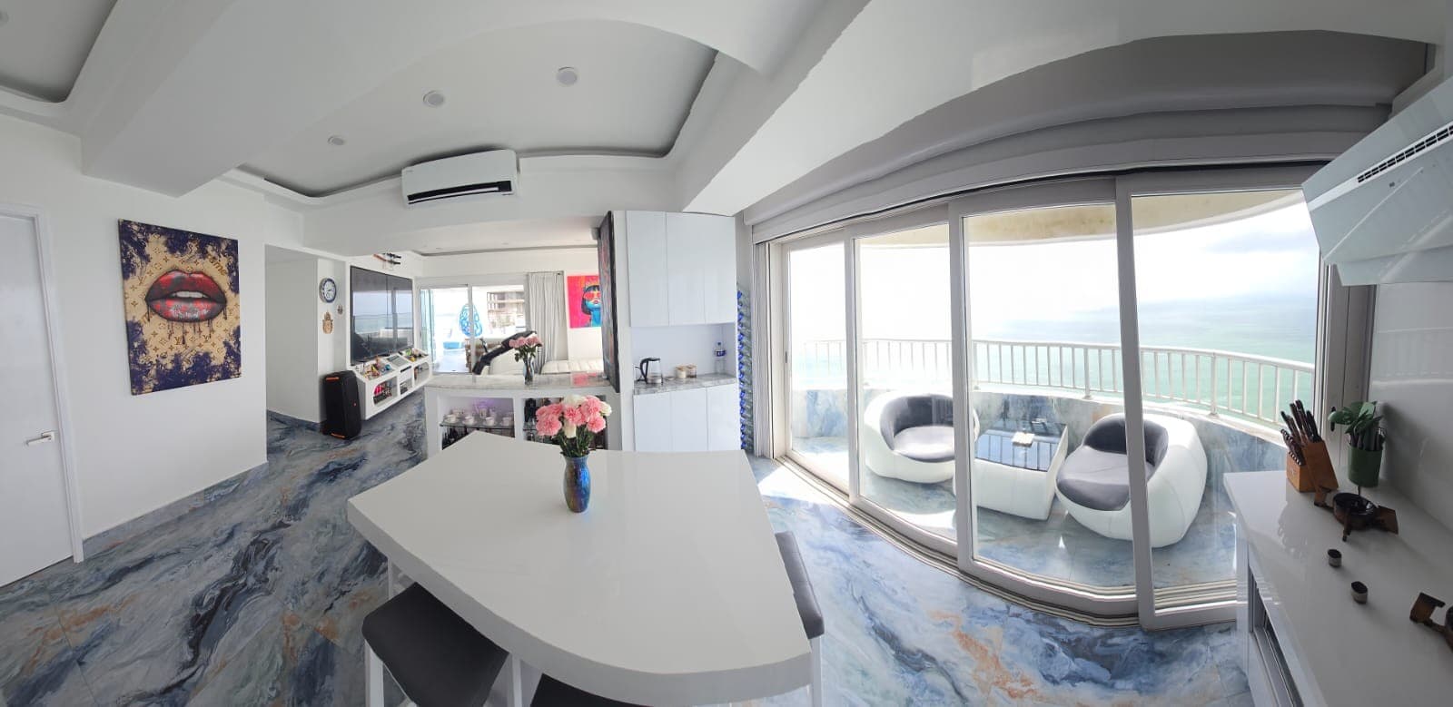 Comedor blanco junto al ventanal, con la terraza y el mar al fondo.
