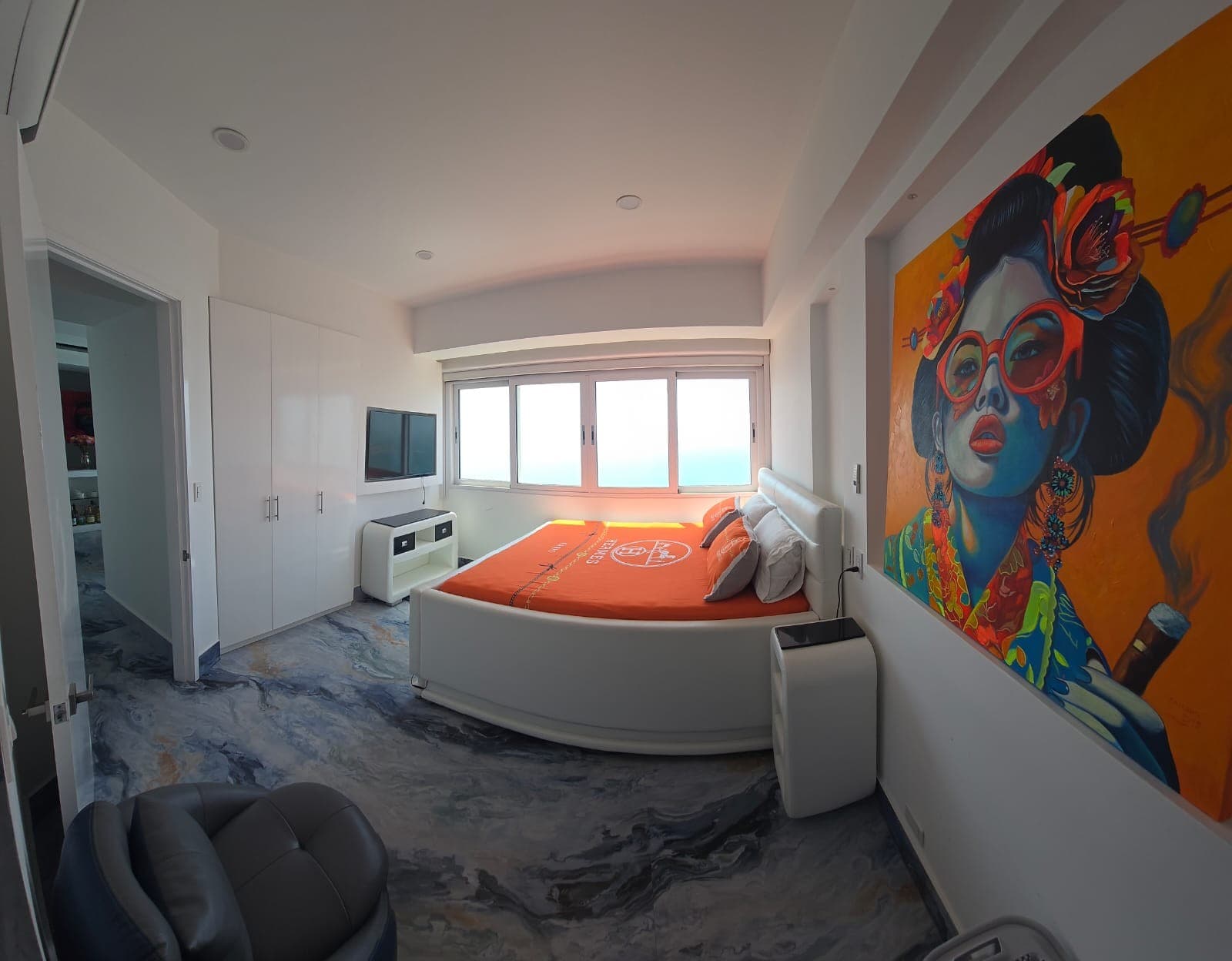 Alcoba con cama redonda, televisor y un mural de gran formato en la pared.