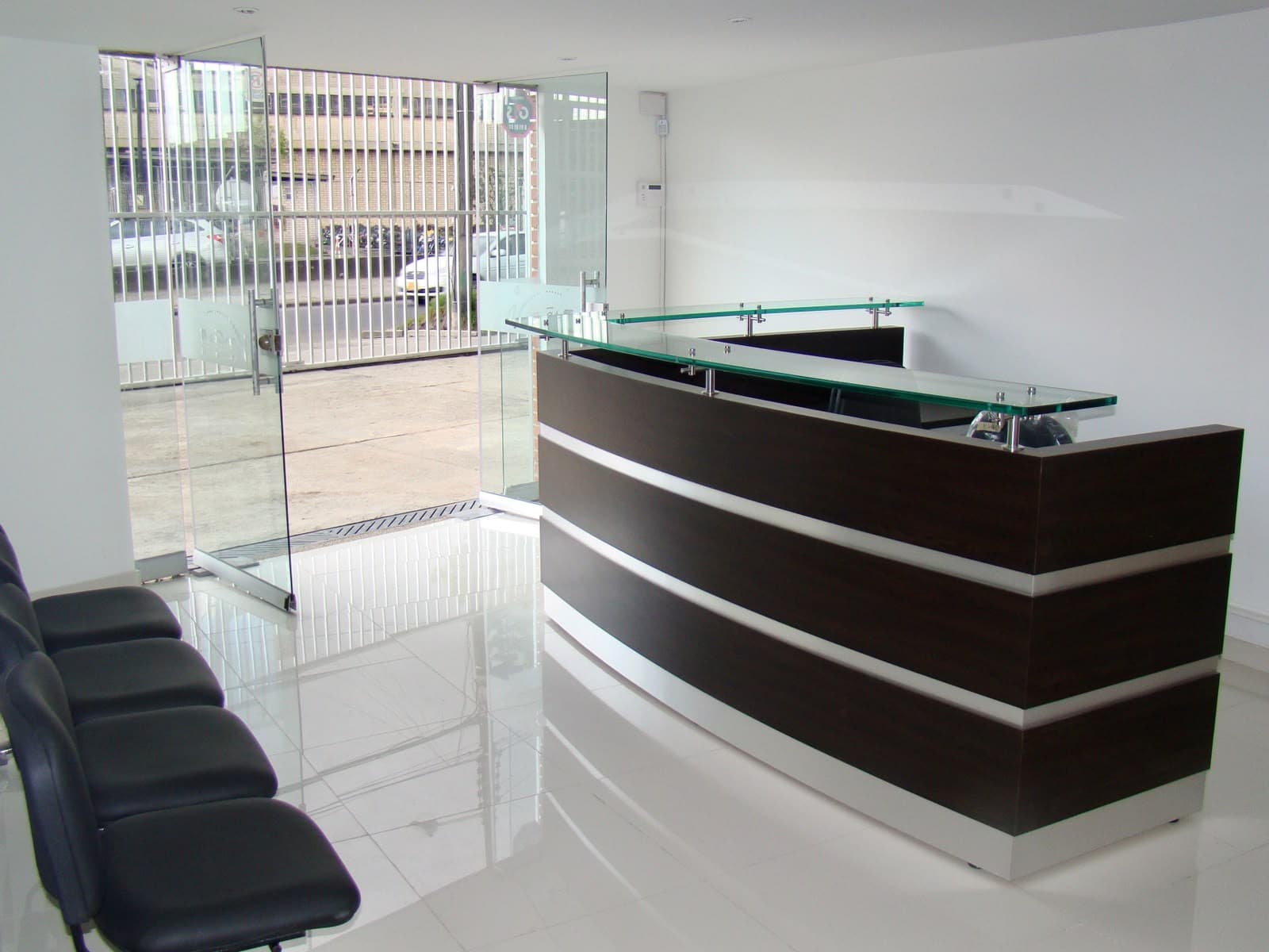 Recepción con mesón en madera y vidrio, y sillas de espera.