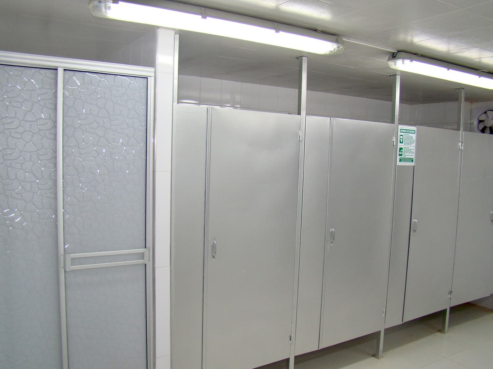 Batería de baños con divisiones y puertas metálicas.