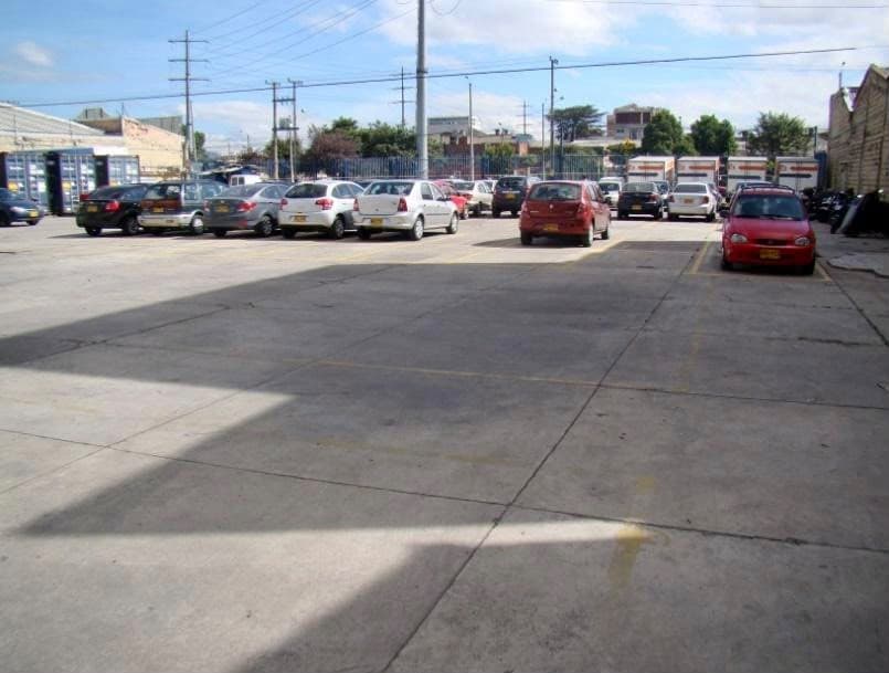 Superficie en concreto del lote con carros parqueados al fondo.