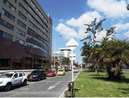 Avenida frente al edificio, con zona verde y árboles.