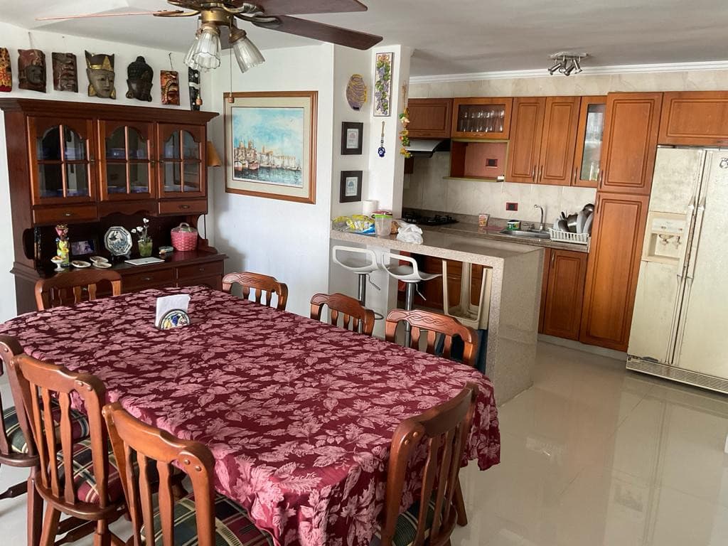 Comedor de madera junto a la cocina, con vitrina y cuadros en la pared.
