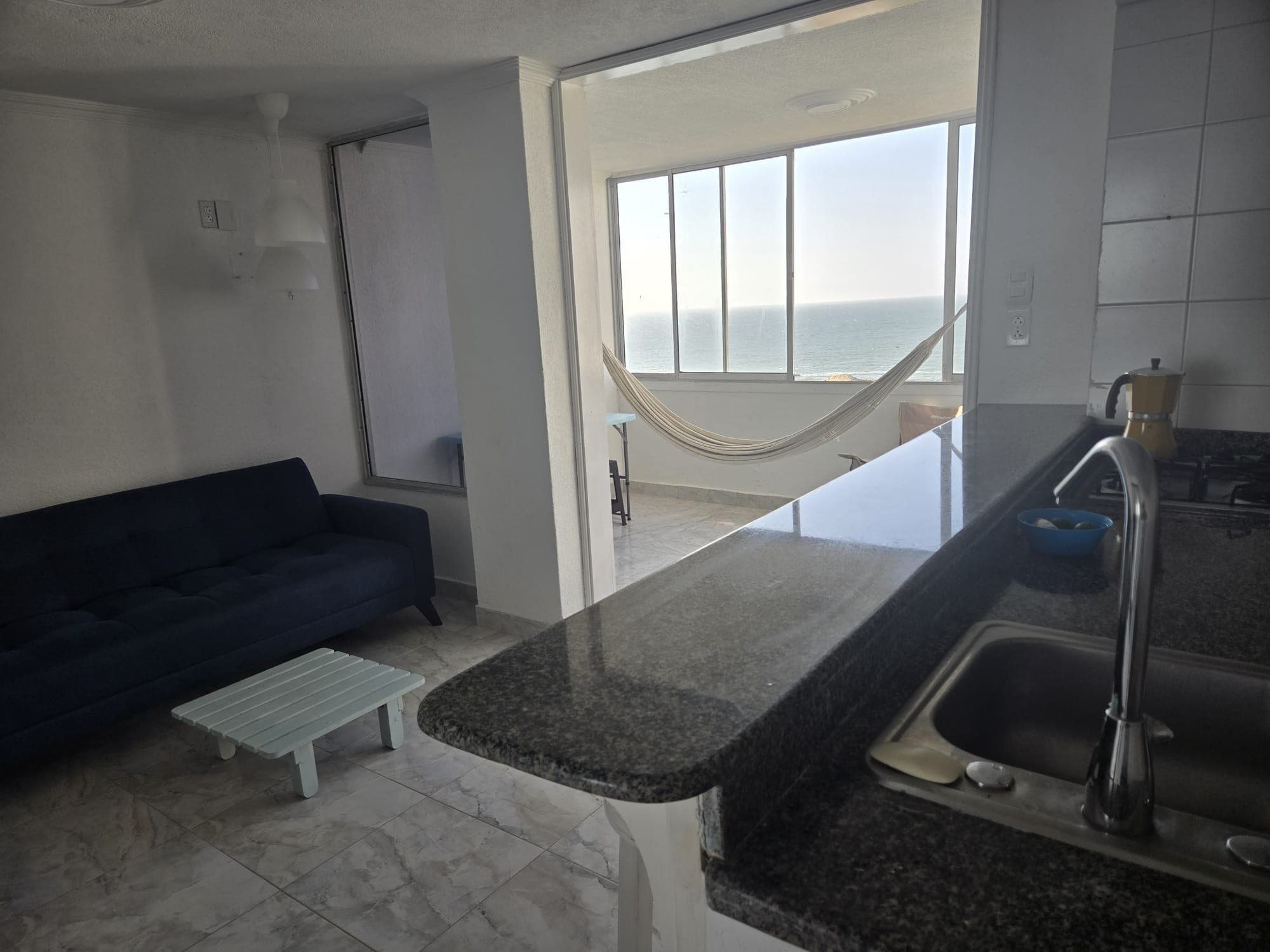 Sala con sofá azul y barra de cocina en granito, con la terraza al fondo.