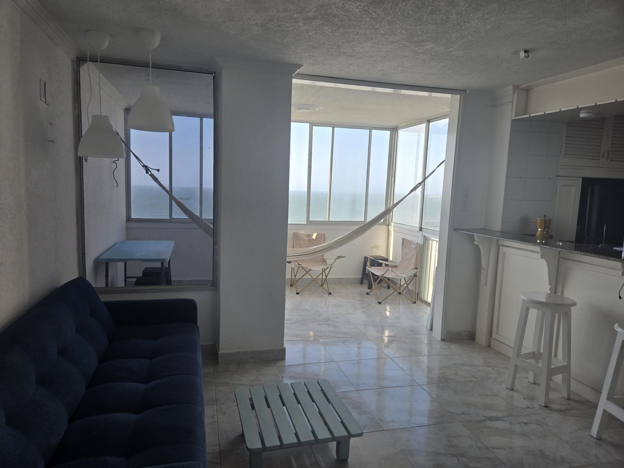 Sala-comedor con sofá azul y la terraza con hamaca al fondo.