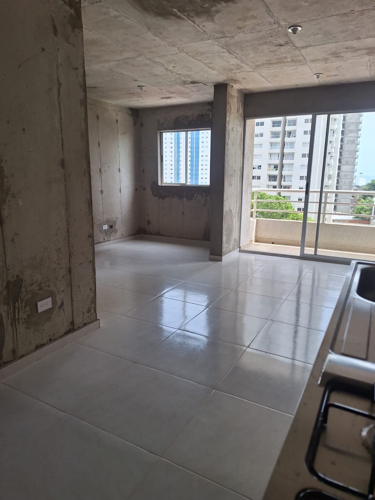 Zona social en obra gris, con piso terminado y ventanal al balcón.