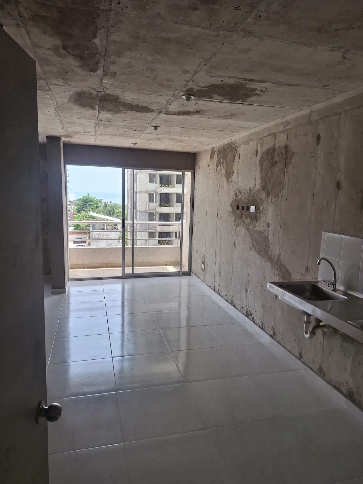 Área de cocina en obra gris, con poceta instalada y salida al balcón.