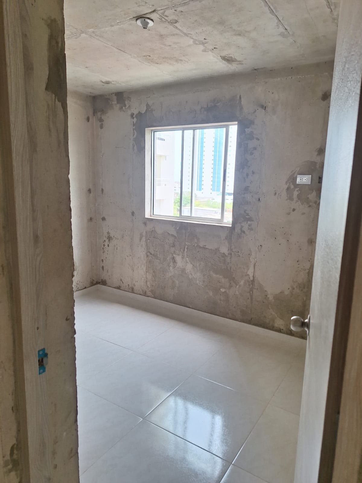 Alcoba en obra gris, con ventana y piso terminado.