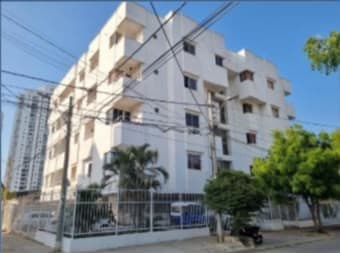 Fachada blanca del edificio de apartamentos, vista desde la calle entre árboles.