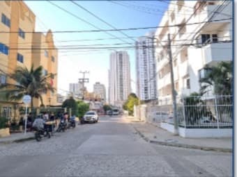 Calle del barrio Torices frente al edificio, con torres al fondo.