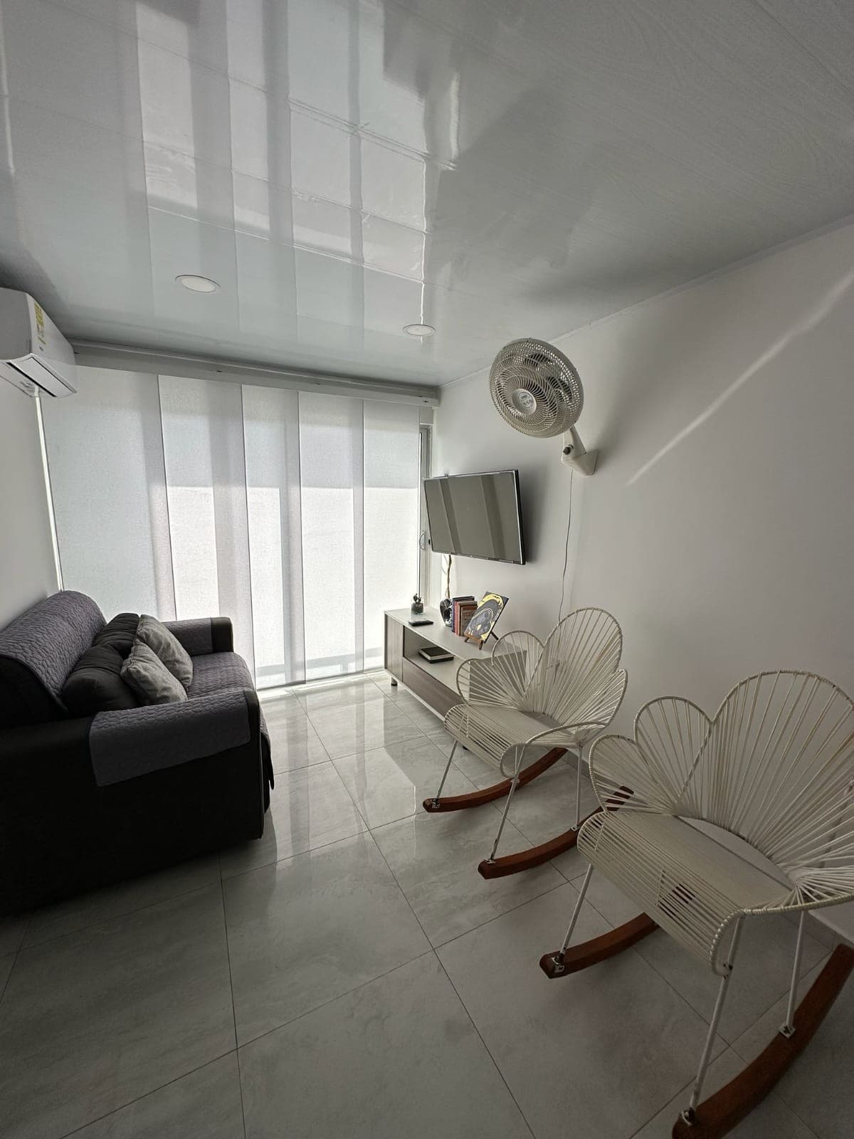 Sala con sofá, mecedoras blancas y ventanal con cortina.